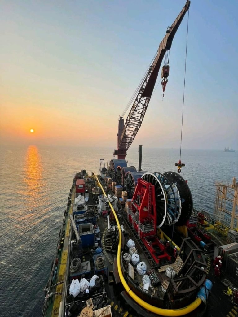 Offshore crew working on cable or hose handling at sunrise on a vessel.